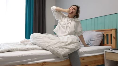 Young Woman Waking Up and Stretching in Her Bedroom Early Morning