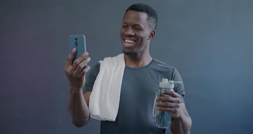 Man Smiling at Phone While Drinking Water