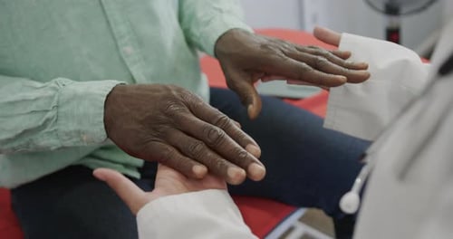 Midsection of diverse female doctor examining male patient in consulting room, slow motion