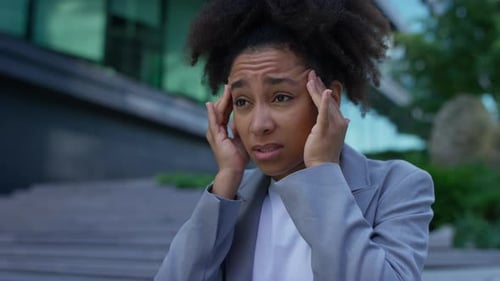Stressed Woman Holds Head Outside Building