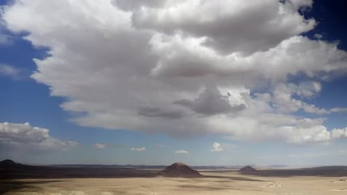 A descending aerial view of an empty and sun-scorched desert landscape with volcanic cones on an ove