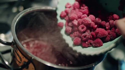 Close-up shot of frozen red raspberries being poured into boiling steamy water. Cooking and healthy