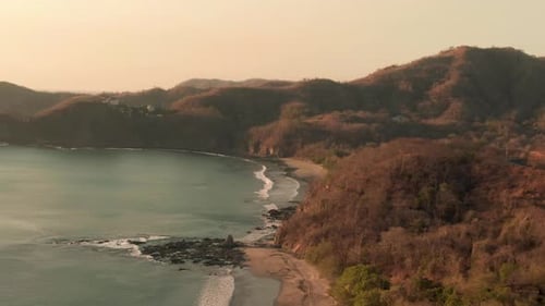 Aerial sunset flight above Flamingo Beach with rock formation and mountain