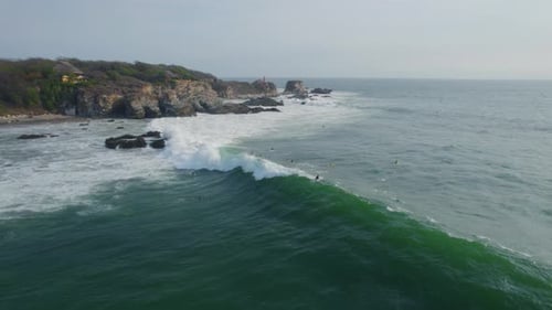 Surfers surfing next to rocks, over Rough sea with waves, Aerial shot from the side.