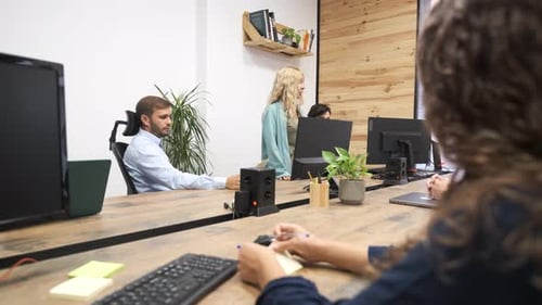 Gerente feminina madura conversando com a equipe sentada em mesas de computador em um escritório criativo
