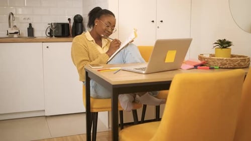 Young Woman Writing at Table with Laptop