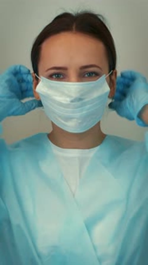 Woman in scrubs putting on a surgical mask