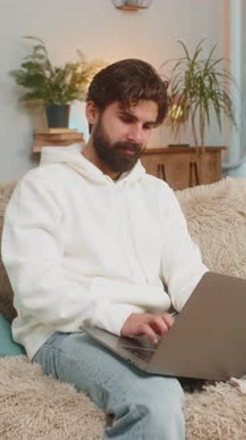 Man with beard sitting on sofa using laptop