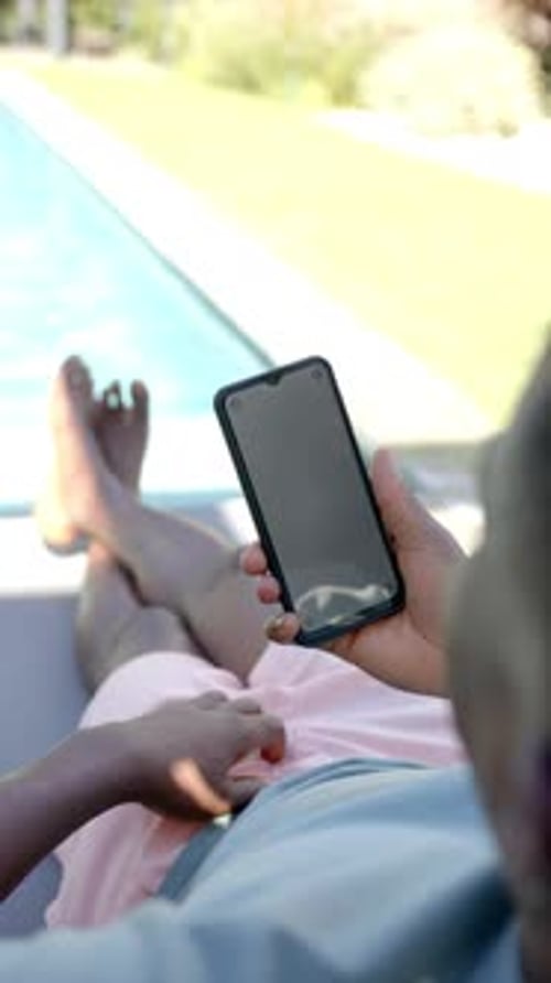Vertical video: Relaxing by pool, person holding smartphone and lounging on chair