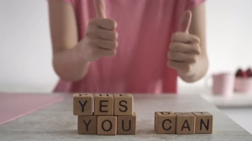 YES, YOU CAN assembled from wooden blocks for motivation. Girl shows positive gesture thumbs up