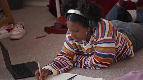 African American Gen Z Girl Doing Homework on Floor in Her Room
