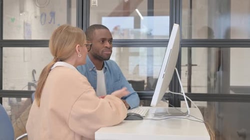 Two Professionals Collaborating on a Desktop Computer in Office
