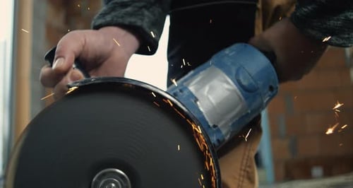 Hand gripping angle grinder during high-speed metal cutting, emitting sparks, close-up on power