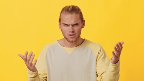 Confused Man Shrugging Shoulders in Front of Yellow Background