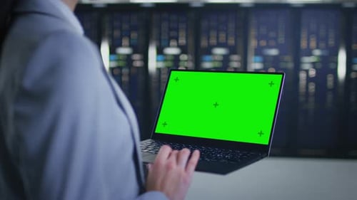Close Up Shot of an IT Specialist Working on Laptop with Mock Up Green Screen in Data Center Next t
