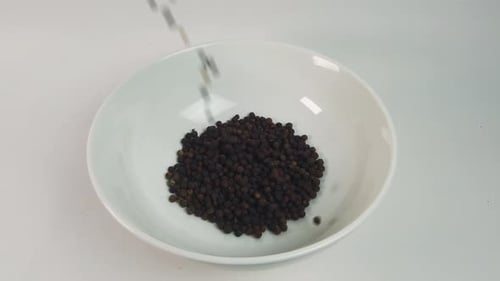 Close up pouring black pepper corn into white bowl. Cooking concept