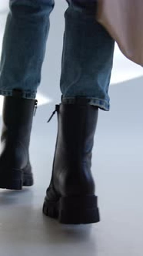 Massive black army boots with laces on a model wearing jeans and beige coat.