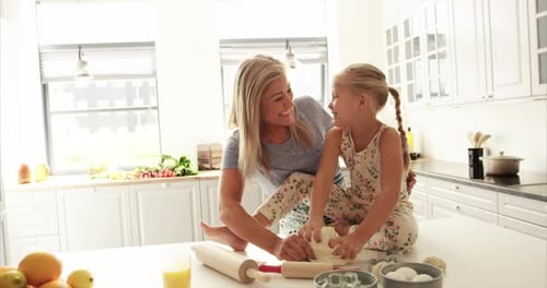 Mother Helping Female Child Seated on Table to Prepare Bread Dough For