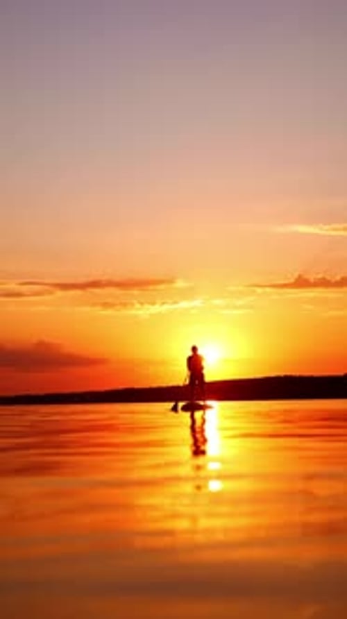 Stunning sunset on the river in summer. One man practicing paddle boarding alone on the calm evening