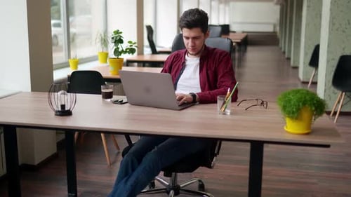 Young Adult Man Working on Laptop in Modern Office