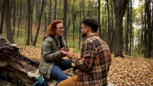 Young couple with backpack drinking tea after hiking in forest.