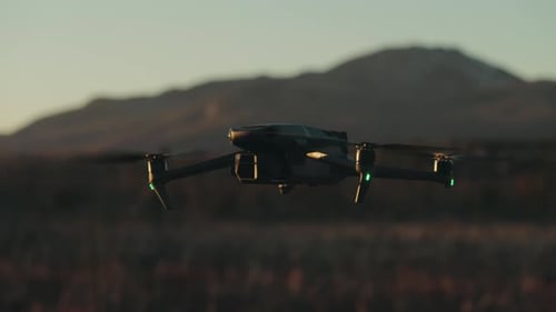 Modern Quadcopter Hovering Over Fields With Bokeh Mountains Background. Selective Focus