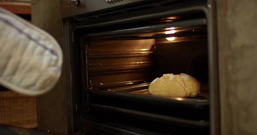 Die Person öffnet die Ofentür in der Küche, greift nach dem Blech und zieht das runde Brot zum Abkühlen heraus