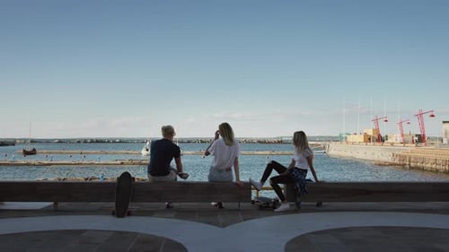 Two Beautiful Girls and Handsome Boy Sitting on the Bench at the Pier and Admiring Harbor with a Se