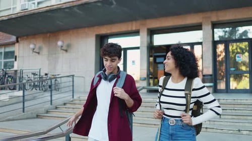 Two multi-ethnic students talk and walk on a sunny university campus.