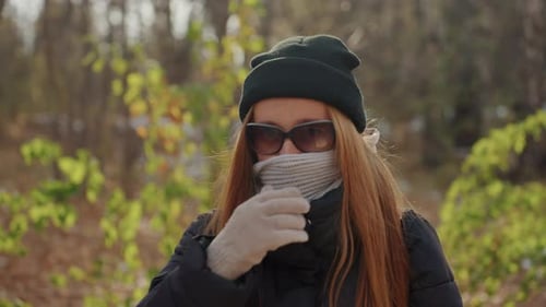 Woman Puts Down Scarf, Smiles in Autumnal Outdoor Setting