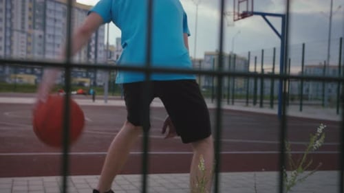 Young Man Training with a Basketball at Sunset on the Court Back View Cinematic