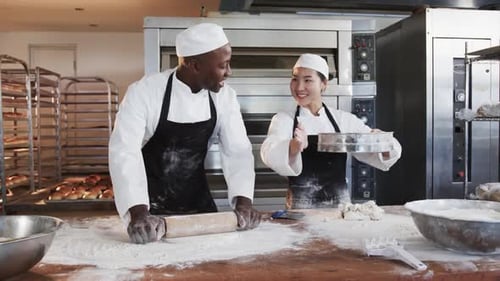 Happy diverse female and male bakers working in bakery kitchen, rolling out dough, slow motion