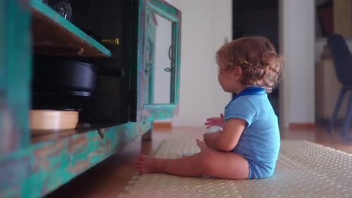 Niño pequeño sentado en el suelo que abre suavemente la rústica puerta del armario mientras estudia el movimiento