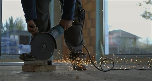 Worker using grinder with flying sparks on construction site, close-up on grinding tool, industrial