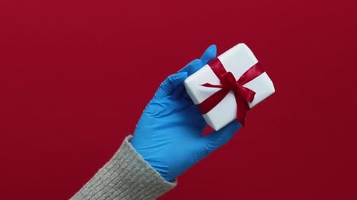 Gloved Hand Holding White Gift Box with Red Ribbon