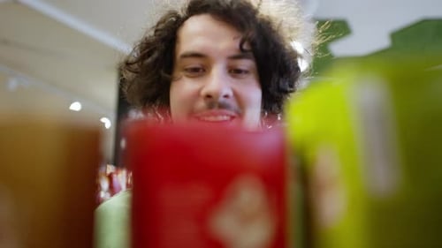 Close Up a Happy Brunette Guy with Curly Hair in a Green Tshirt Chooses the Red Goods He Needs on