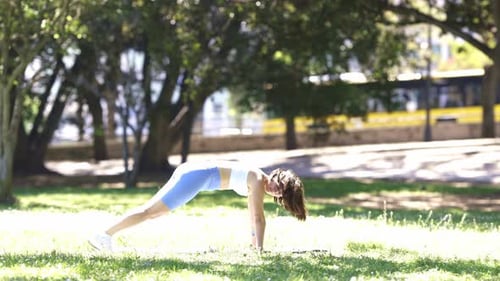 A Woman is Doing a Push Up on a Grassy Field