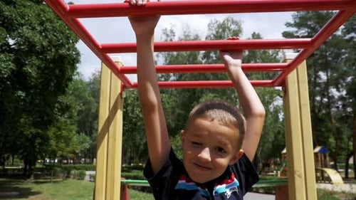 Young Boy Hang on Monkey Bars By His Hands to Exercise at Outdoor Playground Against the Sky in Slow