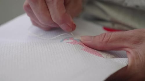 Gros plan d'une main de femme cousant un point de croix.