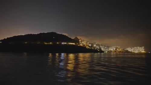 Shot from a boat traveling to the left of an urbanized island in the middle of the night.