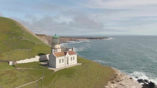Historic lighthouse on coastal cliff side, push in drone shot.