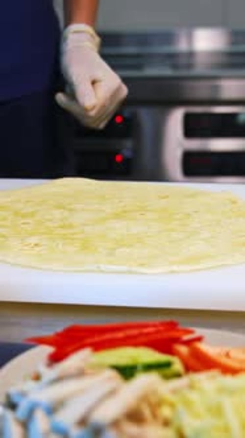 Pita on a table. Man`s hands put white souce on a top. Place with ingredients stand at side.