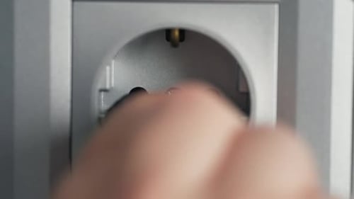 Hand Plugging Black Electrical Cord Into Outlet