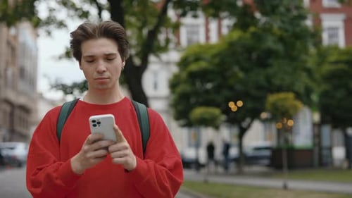 Handsome Caucasian Young Man in Casual Clothes Using Smartphone While Walking on City Street Guy