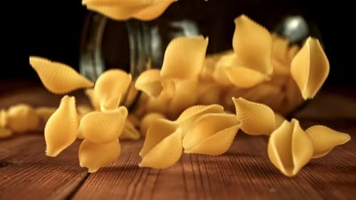 Conchiglie pasta falling on wooden surface in studio