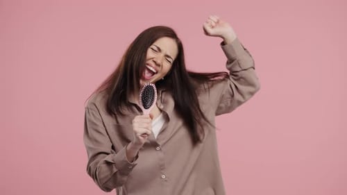 Happy Woman Singing Into Hairbrush On Pink Background
