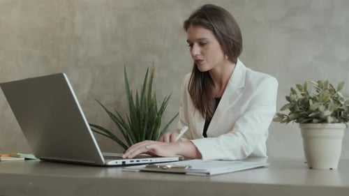 Woman Typing on Laptop and Writing Notes at Desk