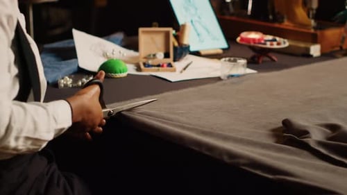 Tailor Cutting Fabric with Scissors at Workspace