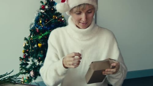 Woman Opening Christmas Gift By Decorated Tree