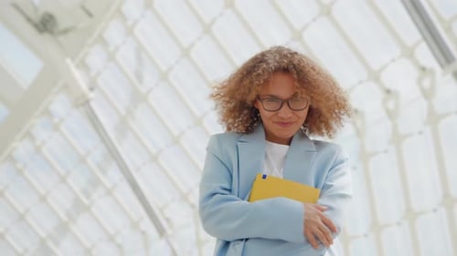 Young Businesswoman with Curly Hair Exuding Confidence in a Modern Interior Holding a Yellow Folder